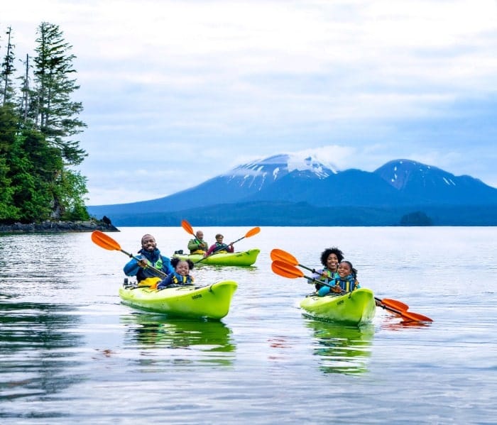 RCI_Alaska_062021_LBlount_D5_Sitka_Kayak_296_RET_V2-min-1 A vibrant outdoor adventure scene featuring multiple bright lime-green kayaks with families
