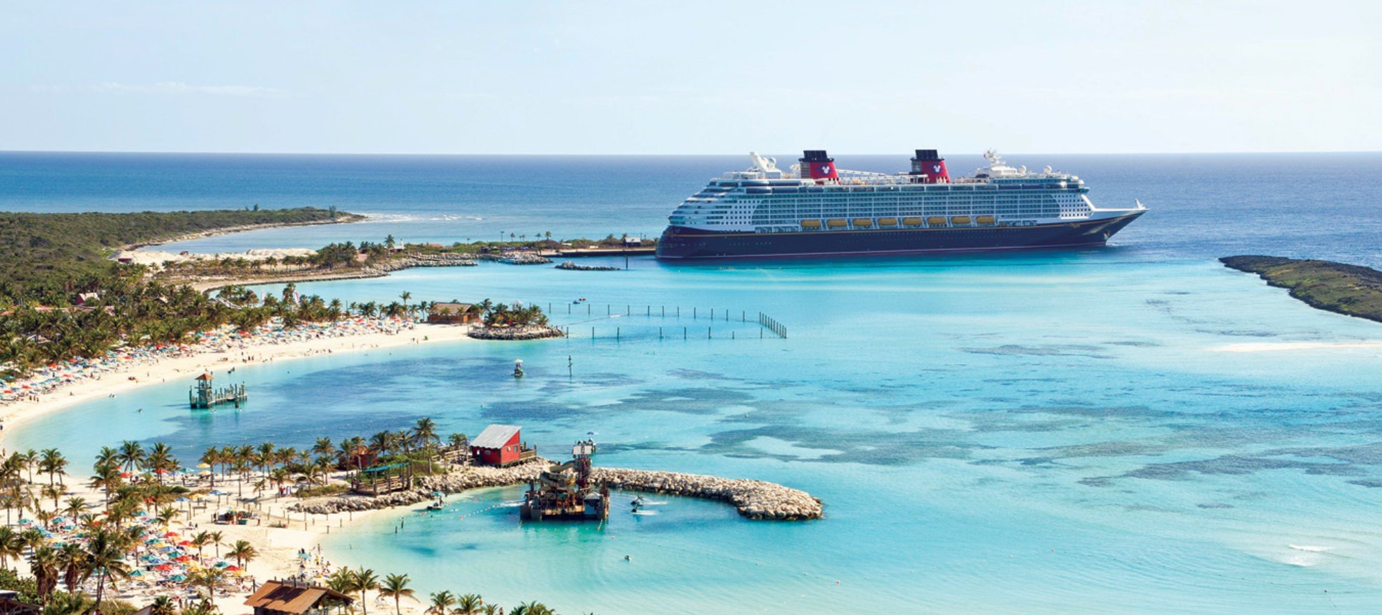 disney-main A large Disney cruise ship anchored off a pristine tropical beach with turquoise waters, palm