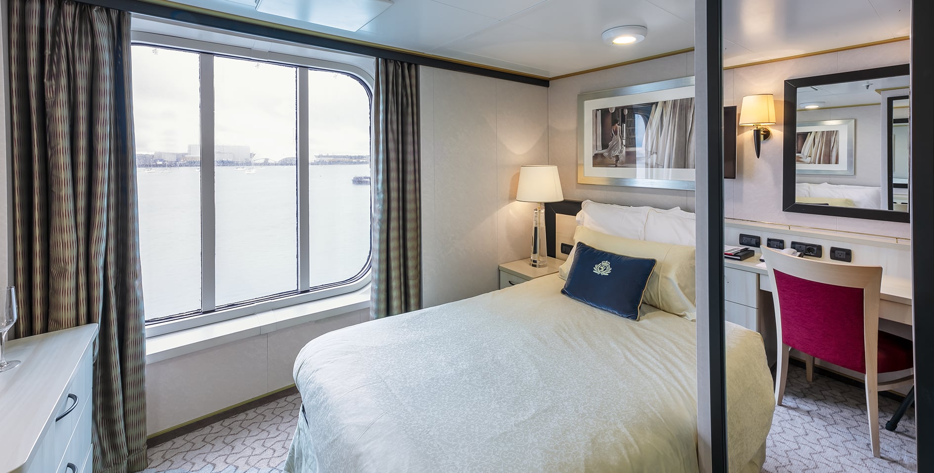 Modern Cruise Ship Sailing Open Ocean A large modern cruise ship with distinctive white and dark blue hull coloring cuts through calm blue ocean waters, leaving a wake behind as it travels. The vessel appears to be a contemporary mega-ship with multiple decks and modern amenities visible from this aerial perspective.