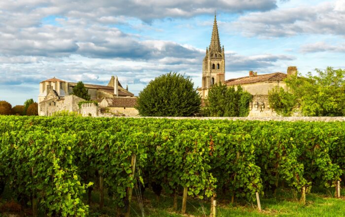Vineyards in Bordeaux, France with a historic stone church and village in the background, showcasing the beauty of France’s wine country often explored on luxury cruising in France itineraries.
