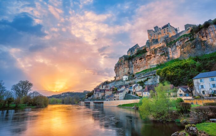 Sunset over the Dordogne River in France with a medieval hilltop castle and riverside village, viewed from the water — a scenic highlight on luxury cruising in France itineraries.