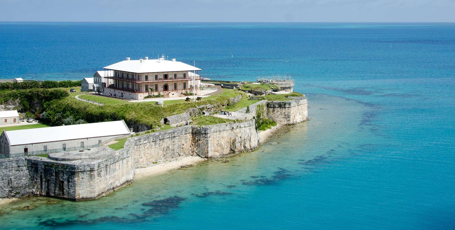 A restored historic fortification with distinctive white roof and stone walls situated on a verdant peninsula overlooking turquoise Atlantic waters. The complex includes period buildings and defensive structures characteristic of Bermuda's colonial military heritage.