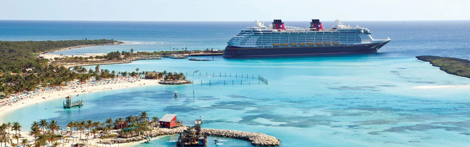 disney-main Large cruise ship anchored in turquoise waters near tropical island beach with palm trees