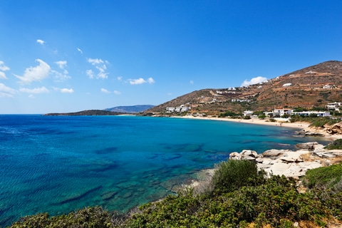 Scenic view of a turquoise bay and hillside village on Andros Island, Greece, with crystal-clear waters and rugged coastline. A Greek island off the beaten path.