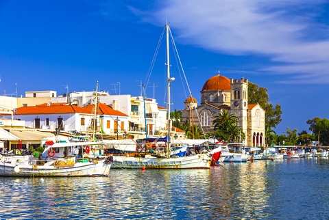 Colorful fishing boats moored in Aegina Harbor with a domed Greek Orthodox church in the background.