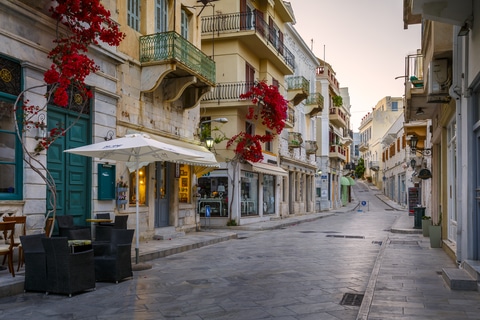 Quiet cobblestone street lined with colorful buildings and blooming bougainvillea in Ermoupoli, Syros, Greece.