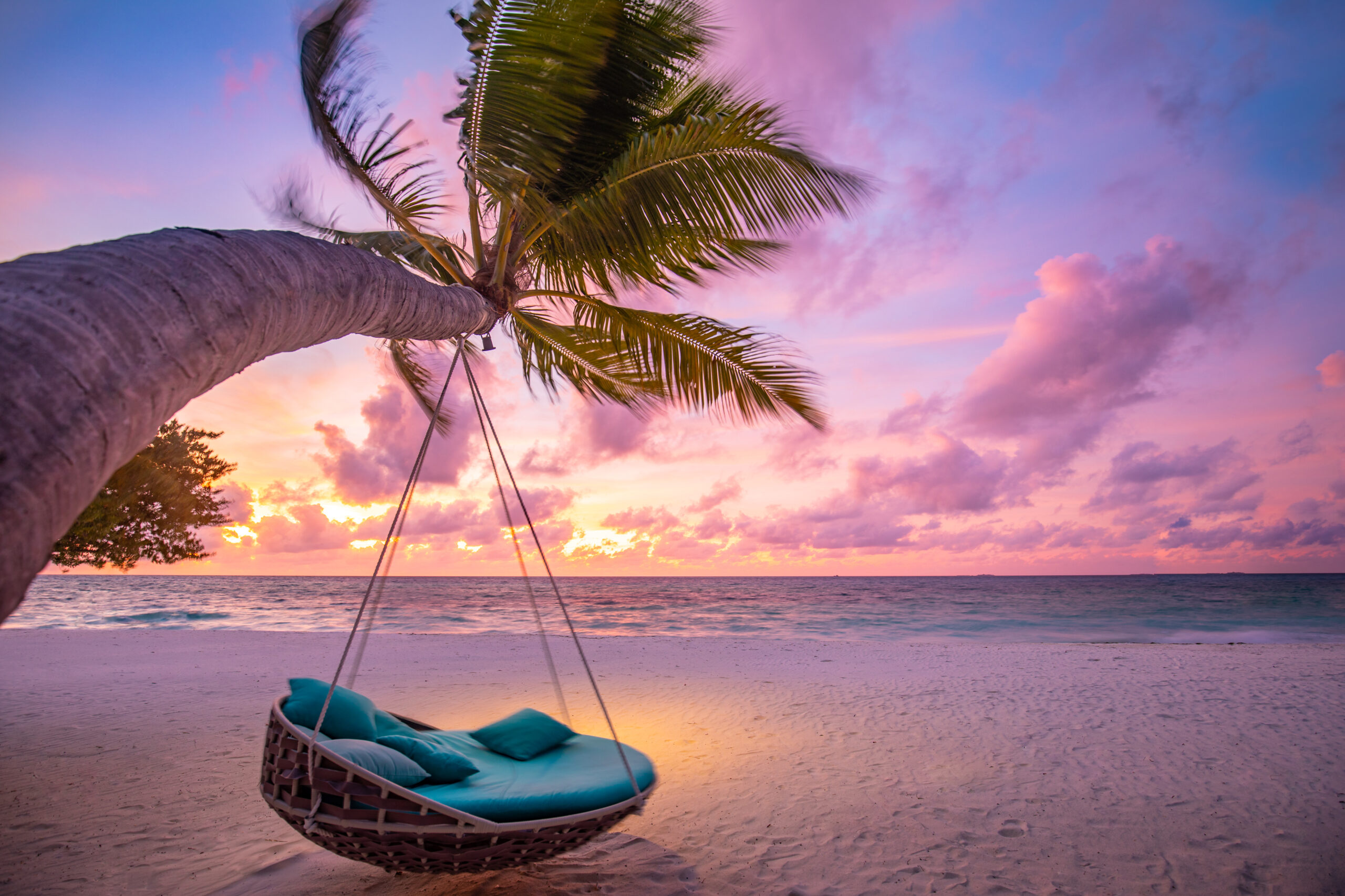 A serene tropical beach scene at golden hour, featuring a suspended swing hanging from a palm tree