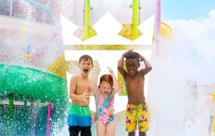 Three children laugh and play under cascading water in a colorful splash zone aboard a Royal Caribbean ship. Multi generational cruise travel.