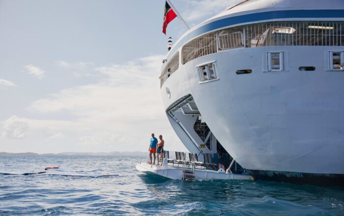 Two travelers stand on the water sports platform of a small cruise ship, surrounded by calm blue seas and distant islands — a serene scene showcasing luxury, adventure, and connection as part of multi-generational travel ideas from Extraordinary Adventures.