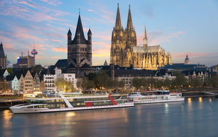 River cruise ship sailing past Cologne Cathedral at sunset along a European itinerary.