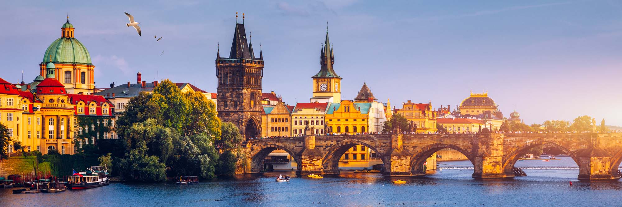 A stunning view of Prague's historic Charles Bridge spanning the Vltava River, featuring medieval architecture, historic towers, and colorful buildings at golden hour.