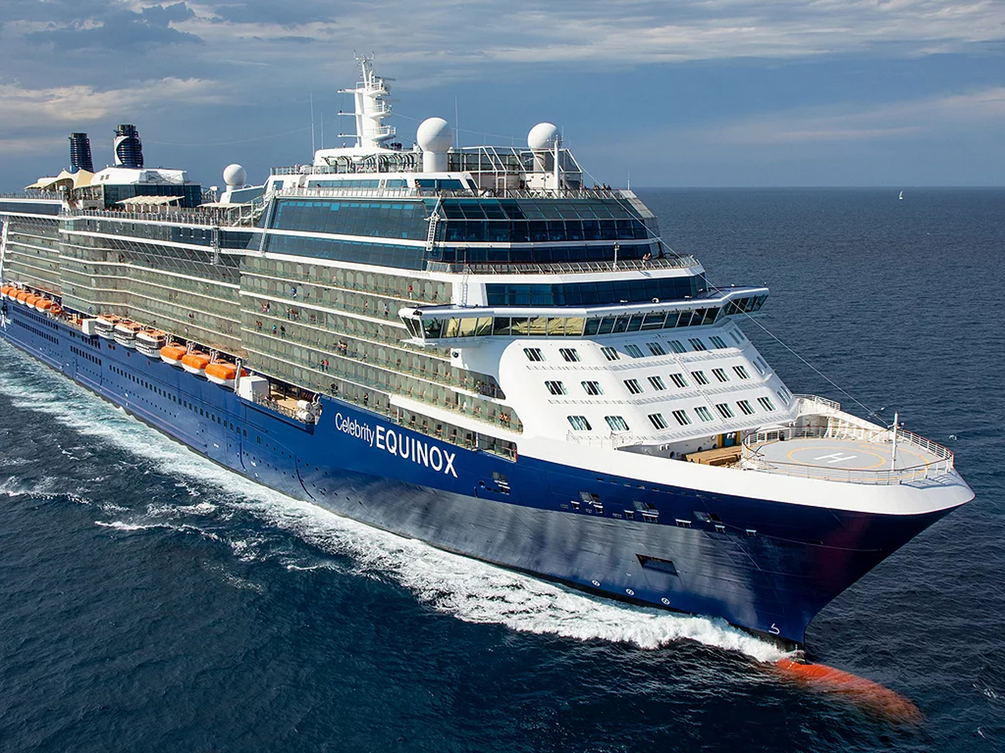 The Celebrity Equinox, a modern luxury cruise ship, sails through open ocean waters under partly cloudy skies. The vessel features the characteristic blue hull and white superstructure of Celebrity Cruises, with multiple decks, satellite domes, and lifeboats visible along its side.