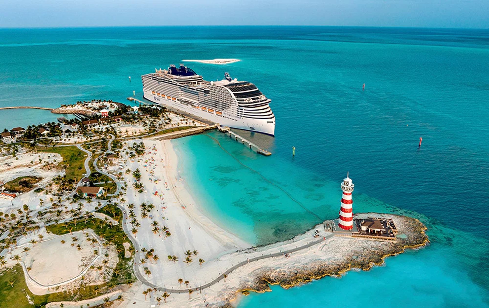 A large modern cruise ship is docked at a pristine tropical island destination featuring a white