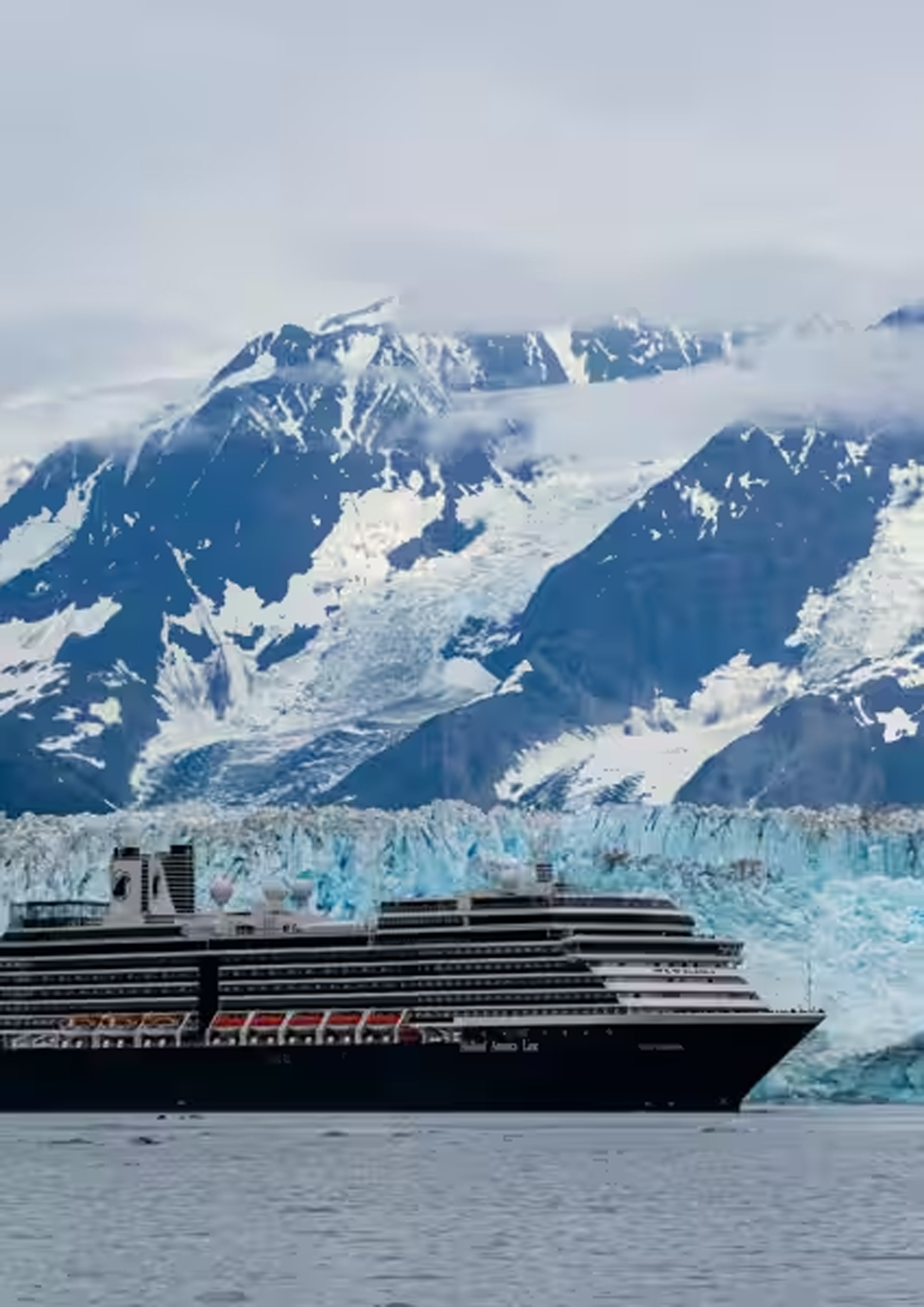 A large modern cruise ship navigates near the stunning Hubbard Glacier in Alaska, with snow-capped mountains and massive blue ice formations towering in the background under a cloudy sky.