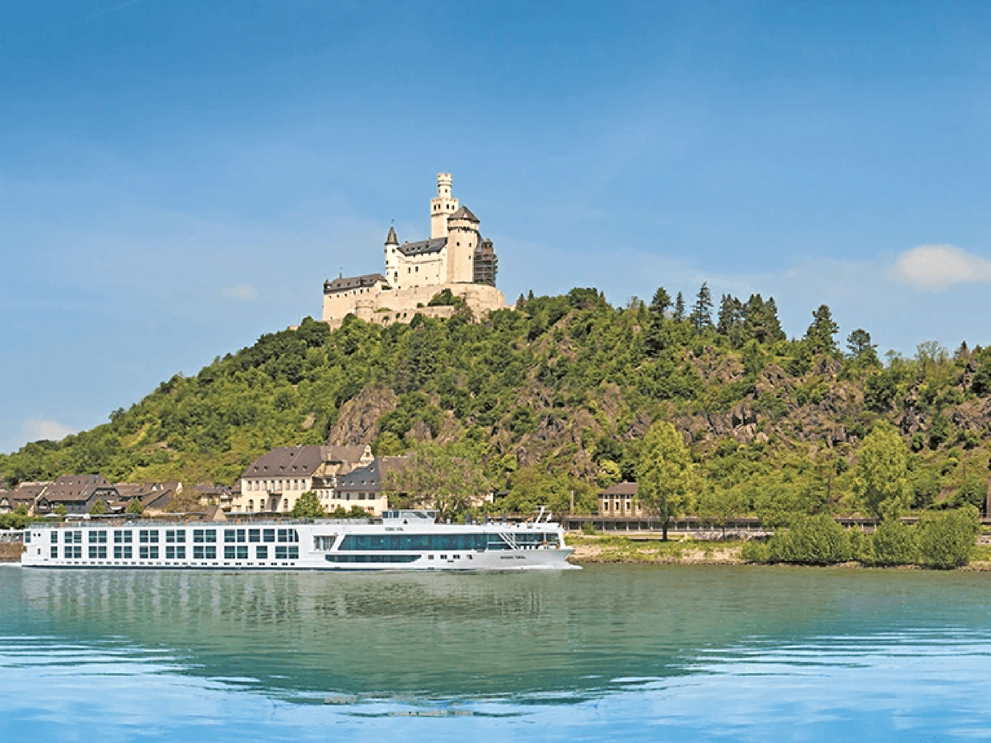 Cruise Ship at Marksburg Castle on Rhine River A modern river cruise ship passes through the Rhine River in Germany with the iconic Marksburg Castle perched dramatically on a forested hilltop in the background. The 12th-century castle's distinctive towers and fortifications rise above the lush green landscape and riverside village below.