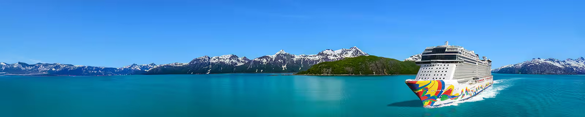 Cruise Ship in Alaskan Mountain Waters A modern cruise ship with distinctive colorful hull livery sails through pristine turquoise waters with snow-capped mountain peaks and a glacier-covered island visible in the background, exemplifying the natural beauty of an Alaskan cruise destination.
