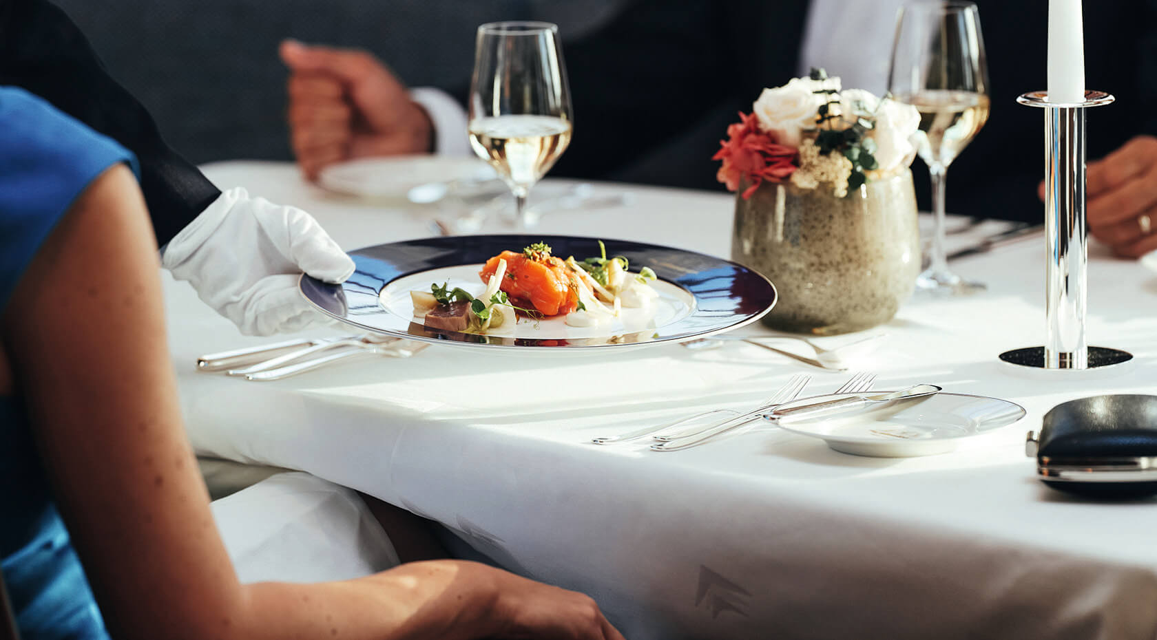 Fine Dining Experience at Sea An elegant fine dining restaurant setting aboard a luxury cruise ship, featuring a beautifully plated gourmet dish with orange and white elements, paired with white wine, fresh floral centerpiece, and impeccable table settings with formal linens and candlelight.