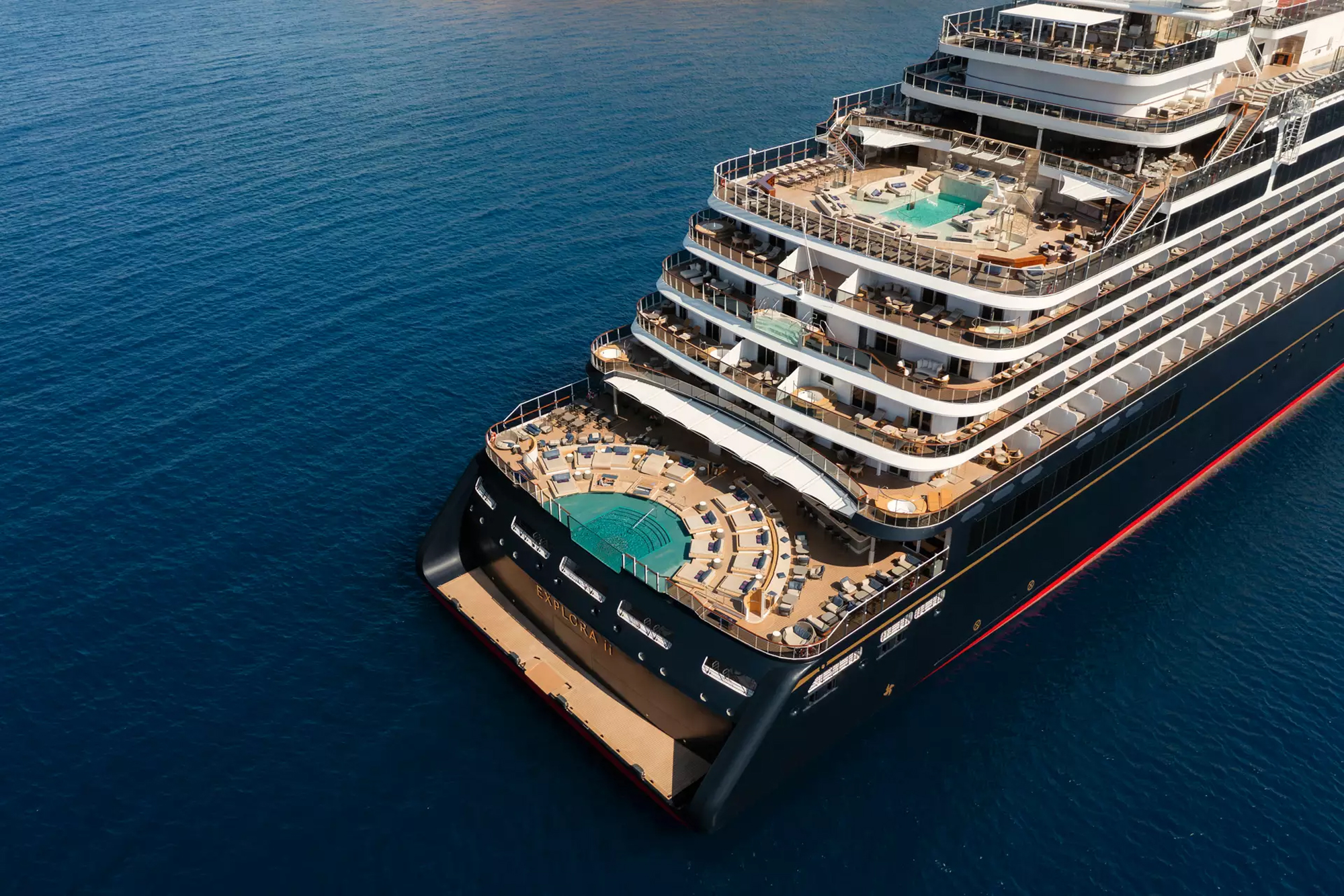 Luxury Cruise Ship Aerial Pool Deck View An aerial photograph of a large modern cruise ship featuring multiple swimming pools, sun decks with lounge chairs, and multiple tiered passenger decks. The vessel is positioned in clear blue water, showcasing its impressive size and luxurious amenities from above.