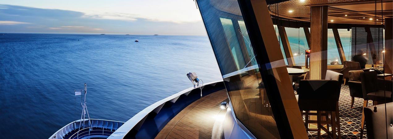 A panoramic view from a modern cruise ship's observation deck, showcasing expansive blue ocean waters and an elegant interior lounge with large glass windows.