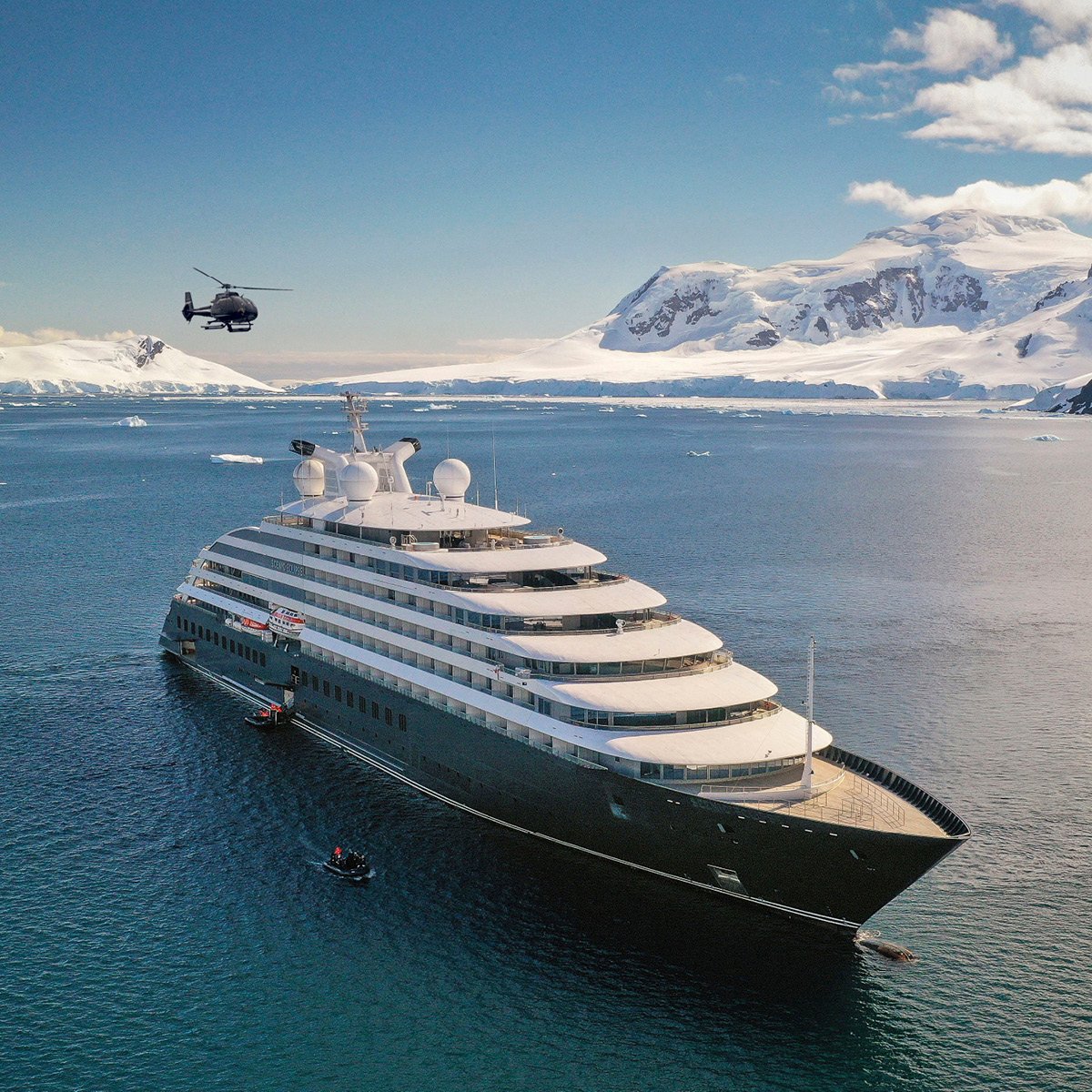 Luxury Cruise Ship in Antarctic Waters A large expedition cruise ship anchors in pristine Antarctic waters surrounded by snow-capped mountains and glaciers, with a helicopter hovering above and zodiac boats nearby for shore excursions.