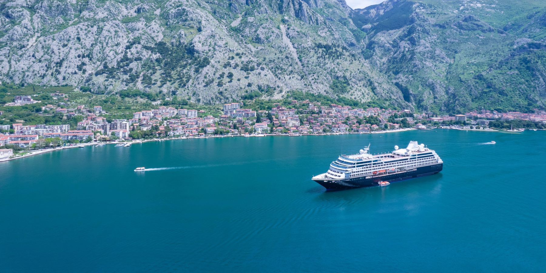 A modern luxury cruise ship anchors in crystal-clear turquoise waters beneath dramatic limestone