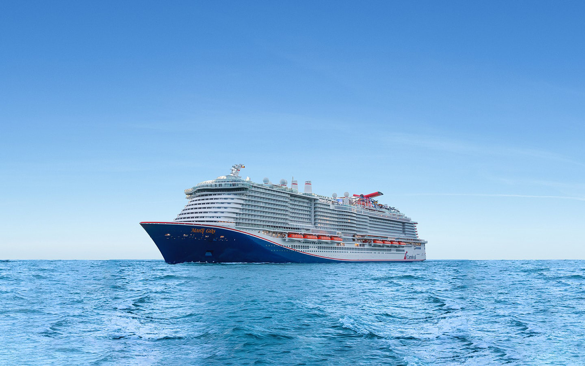 A large modern cruise ship with distinctive dark blue hull and white superstructure sails on clear blue ocean waters under a bright, cloudless sky. The vessel features red accent details and multiple deck levels, representing contemporary cruise ship design.