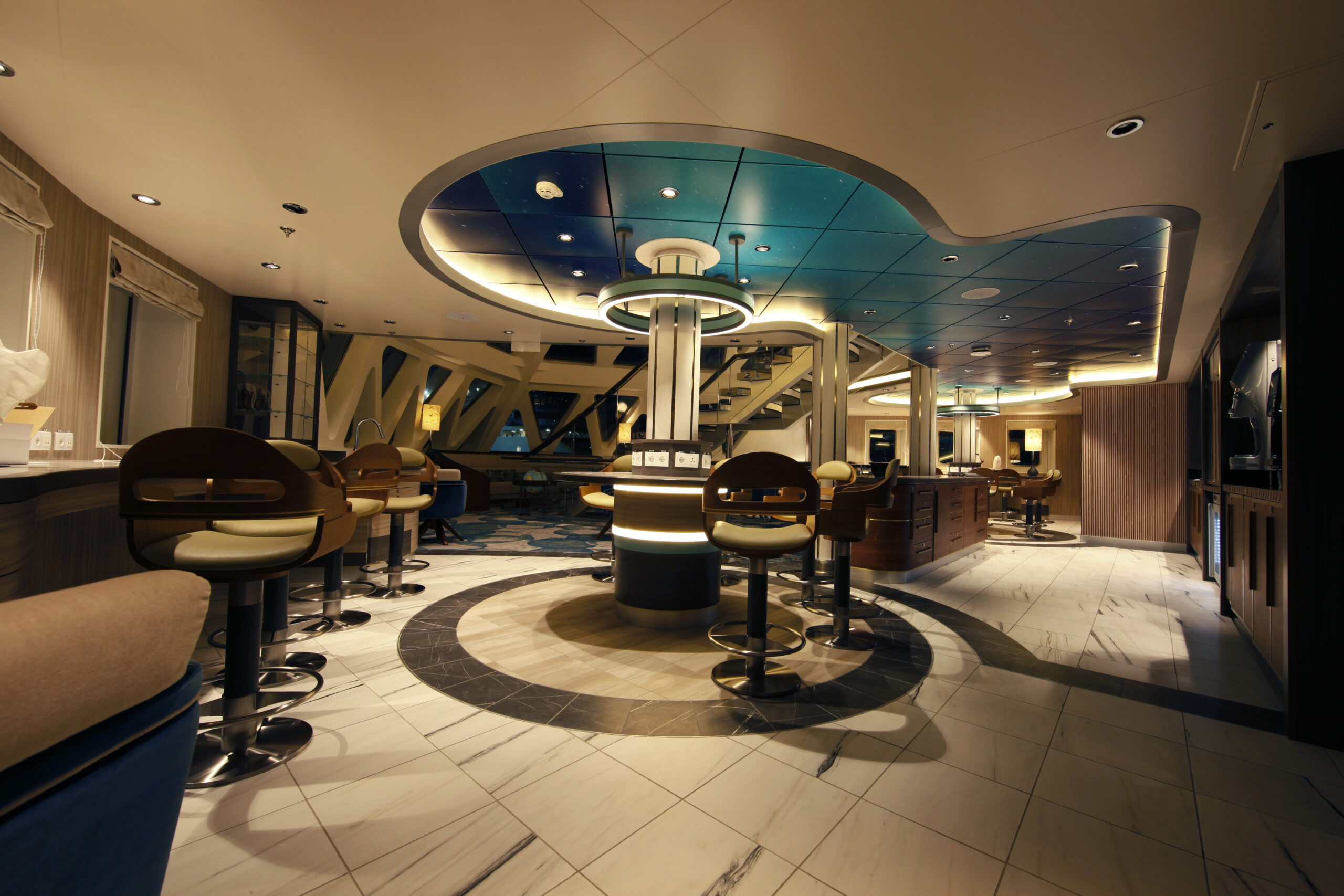 Modern Cruise Ship Science Centre Lounge A contemporary lounge and science center aboard a cruise ship, featuring sophisticated interior design with curved architectural elements, ambient lighting, comfortable seating areas with brown leather chairs, and a striking teal-colored ceiling with integrated lighting fixtures. The space demonstrates modern luxury cruise ship amenities and hospitality design.