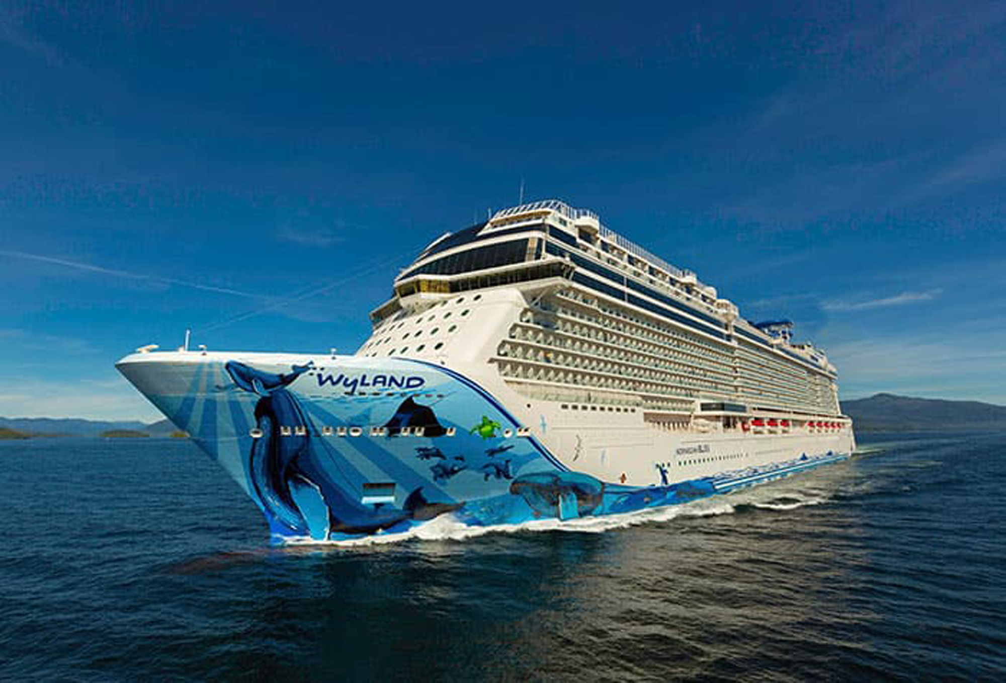 Norwegian Bliss Cruise Ship at Sea A modern cruise ship with distinctive blue whale artwork on its hull sails through clear blue waters under a bright sky. The vessel features multiple decks with balconies and a sleek white superstructure, characteristic of contemporary cruise ship design.