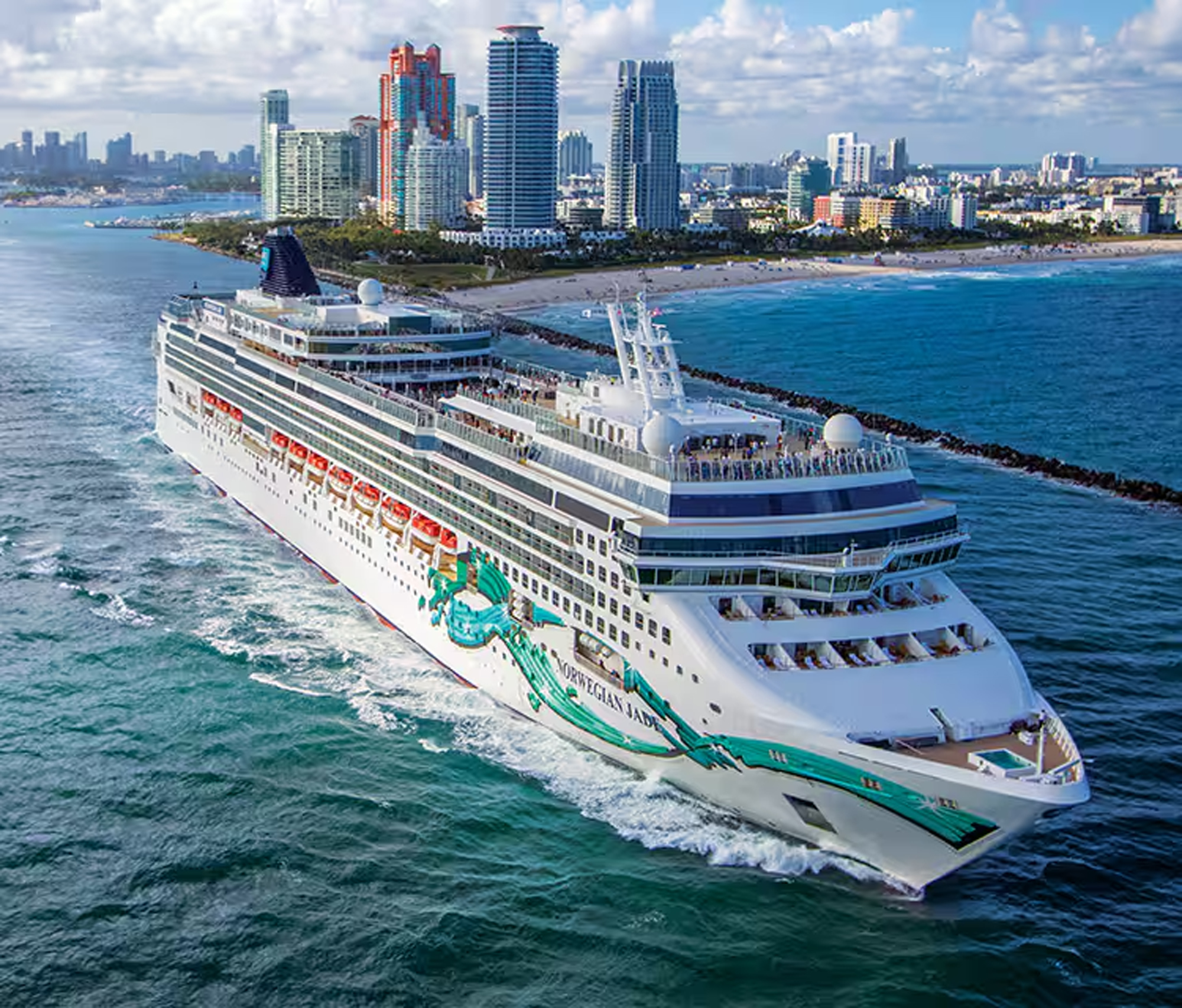Norwegian Jade Cruise Ship at Miami Beach The Norwegian Jade, a large modern cruise ship with distinctive green and white livery, sails off the coast of Miami Beach, Florida. The vessel is shown in clear daylight with the iconic Miami skyline and colorful Art Deco hotels visible in the background, showcasing the ship's impressive scale against the urban beachfront landscape.