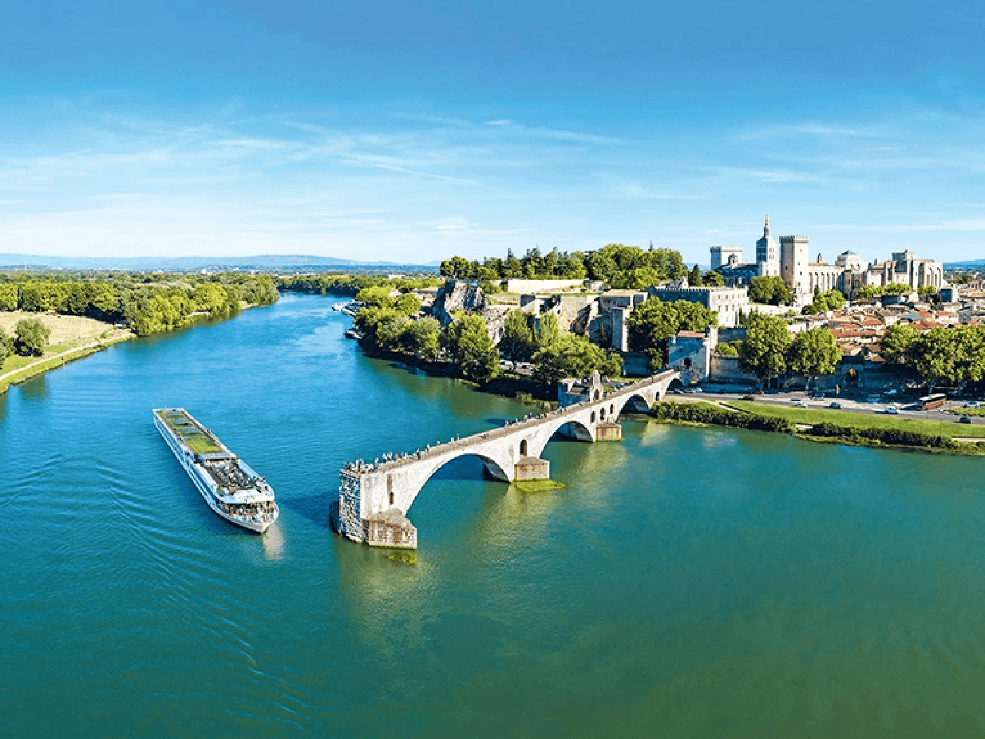 Scenic Sapphire Cruising Through Avignon A river cruise ship navigates the Rhône River in Avignon, France, passing beneath the iconic 12th-century Saint-Bénézet Bridge with the historic papal palace and medieval city skyline visible on the right bank. The scene captures the picturesque medieval architecture and lush riverside landscape characteristic of Provence.