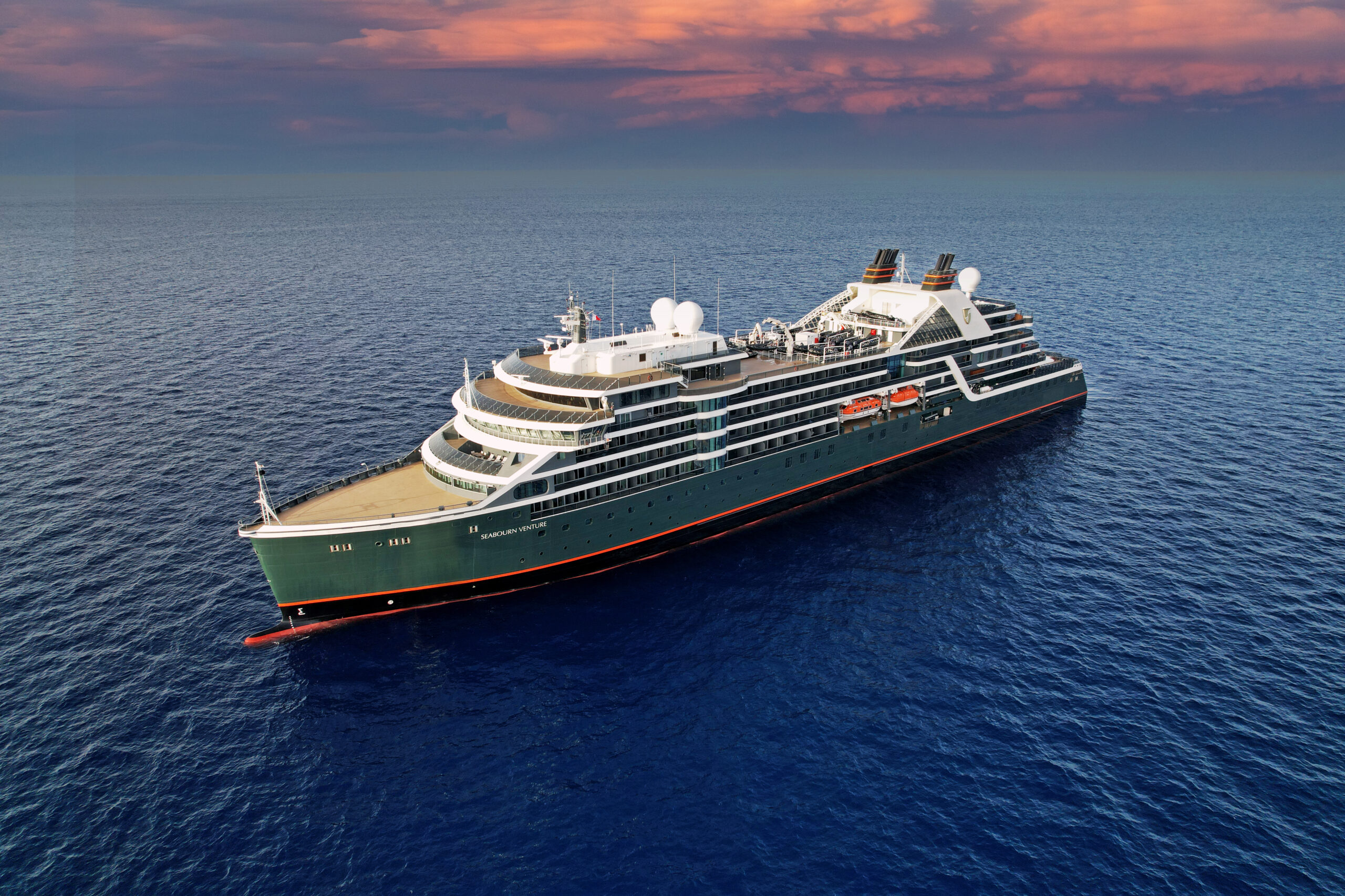 A luxury expedition cruise ship with distinctive green hull and white superstructure sailing in calm blue waters during golden hour. The vessel features modern tiered decks with multiple white domes and visible lifeboats, characteristic of premium small-ship cruising designed for remote destinations.