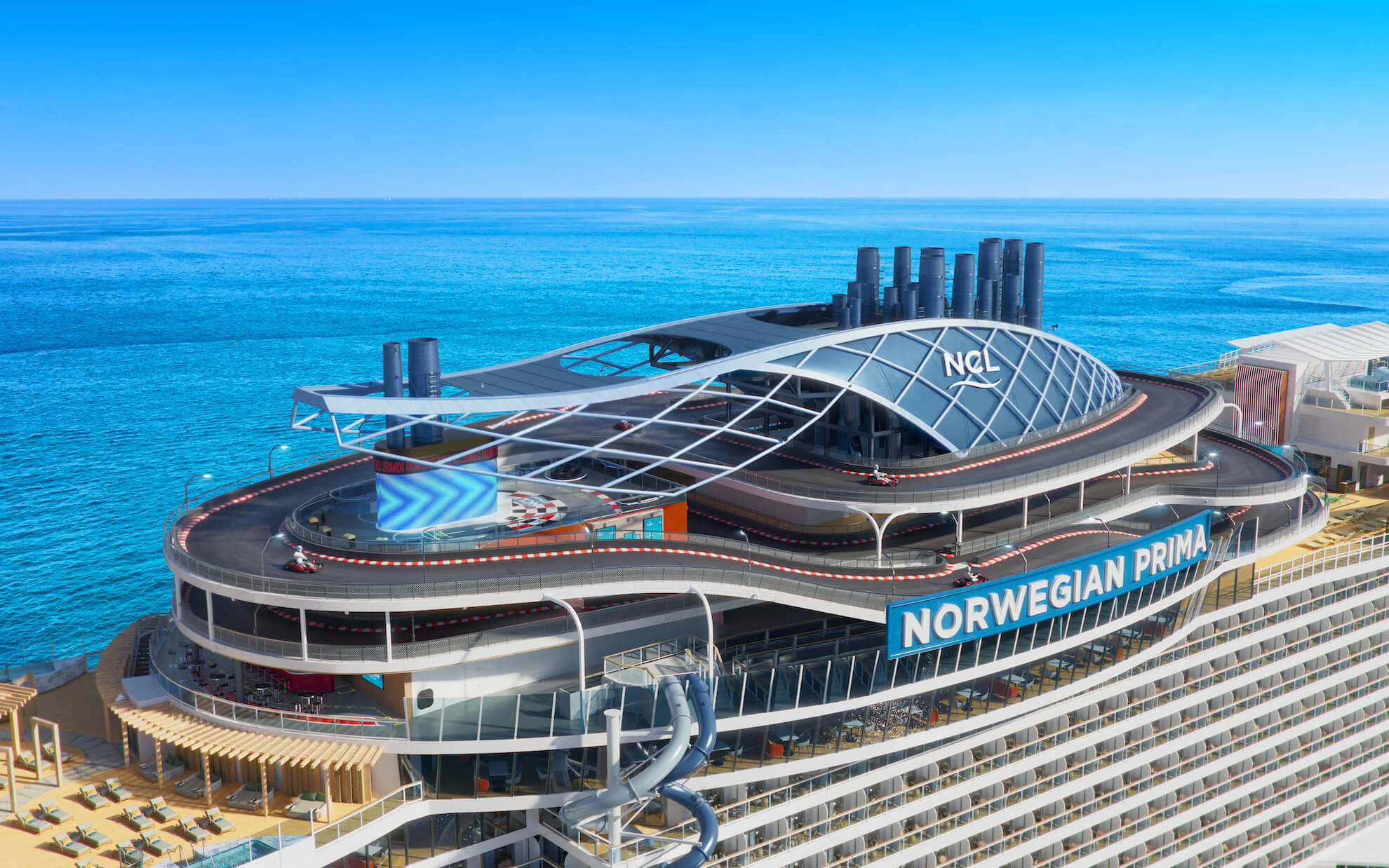 norwegian-cruise-line-prima-aerial-speedway-1 An aerial view of the Norwegian Prima cruise ship docked at port, showcasing its distinctive modern architecture with a curved, grid-patterned roof structure over the promenade deck. The vessel features multiple tiers of accommodations and entertainment venues overlooking sparkling blue waters.