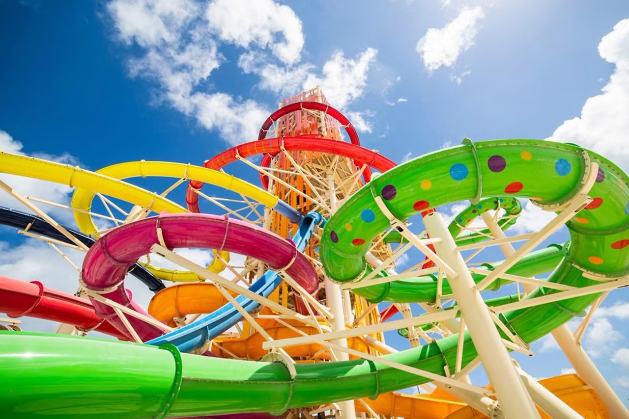 A vibrant water park scene featuring multiple colorful tube slides in bright green, pink, yellow
