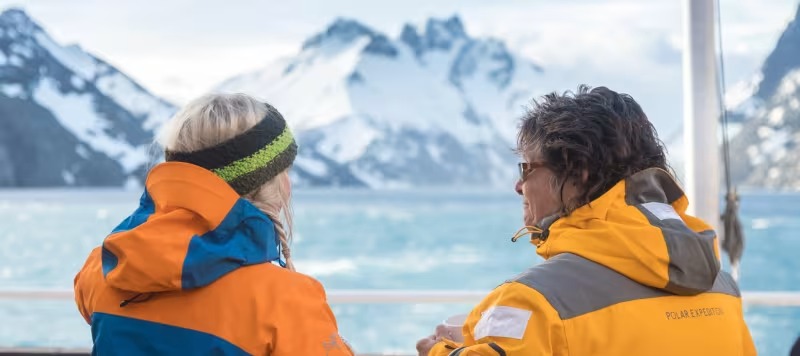 Glacier Bay Expedition Cruise Passengers Two passengers in orange life jackets viewing snow-capped mountains in Glacier Bay