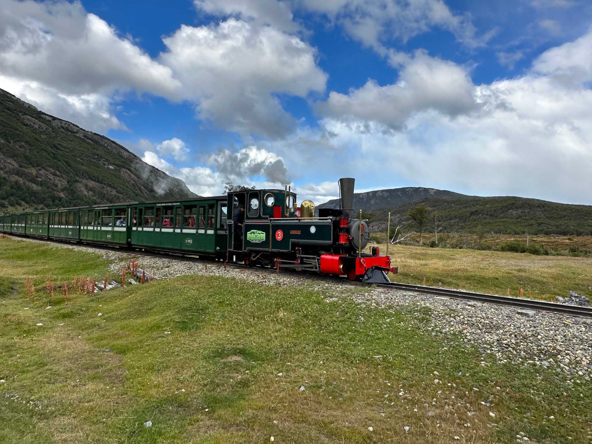 A vintage steam locomotive with black boiler and red accents pulls green passenger cars across
