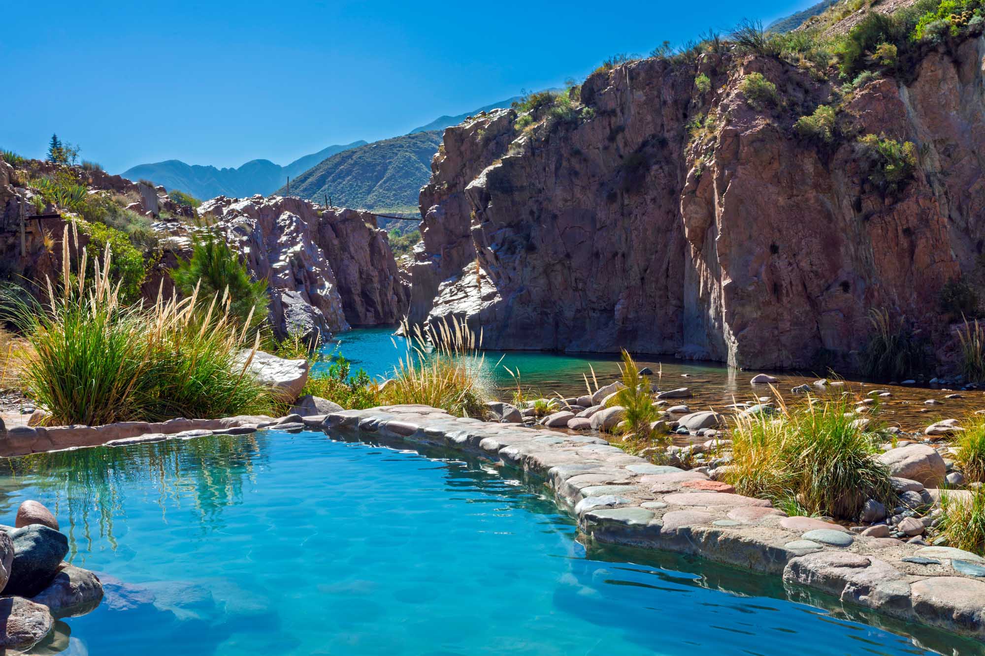 A stunning natural hot springs pool nestled between dramatic red rock cliffs with crystal-clear