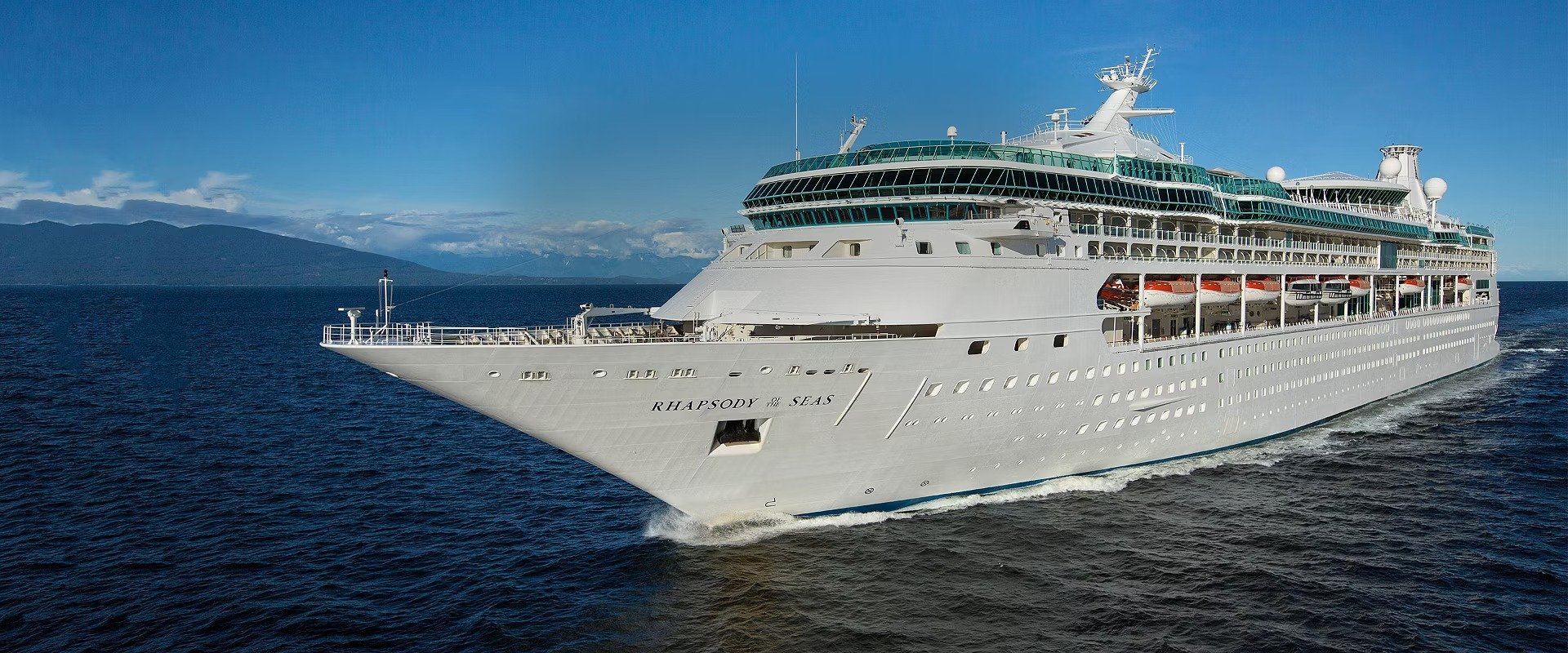 Rhapsody of the Seas Cruising in Alaska Rhapsody of the Seas cruising through Alaska's pristine blue waters with mountains in background