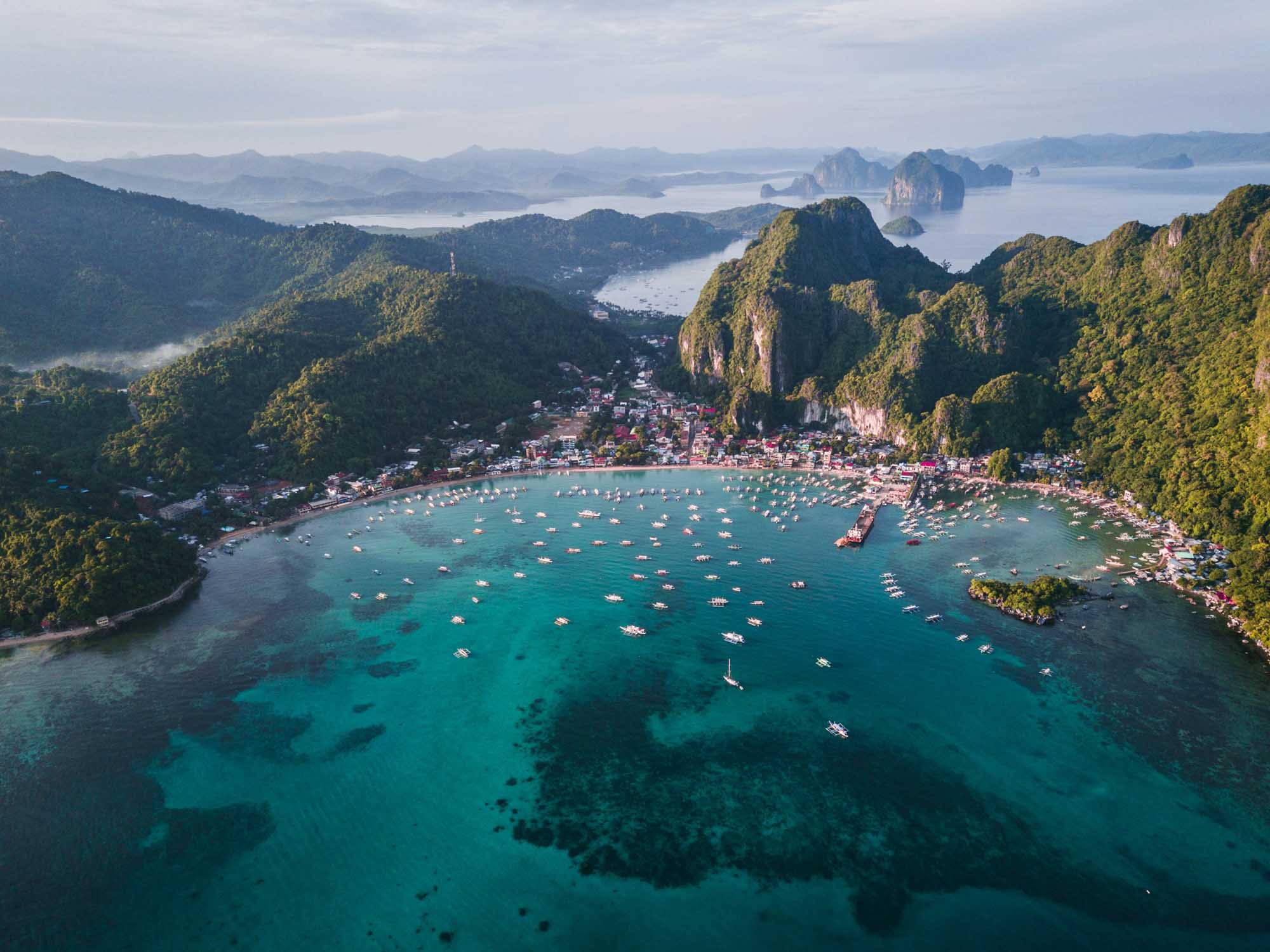 An aerial view of a pristine turquoise bay surrounded by dramatic limestone cliffs and lush