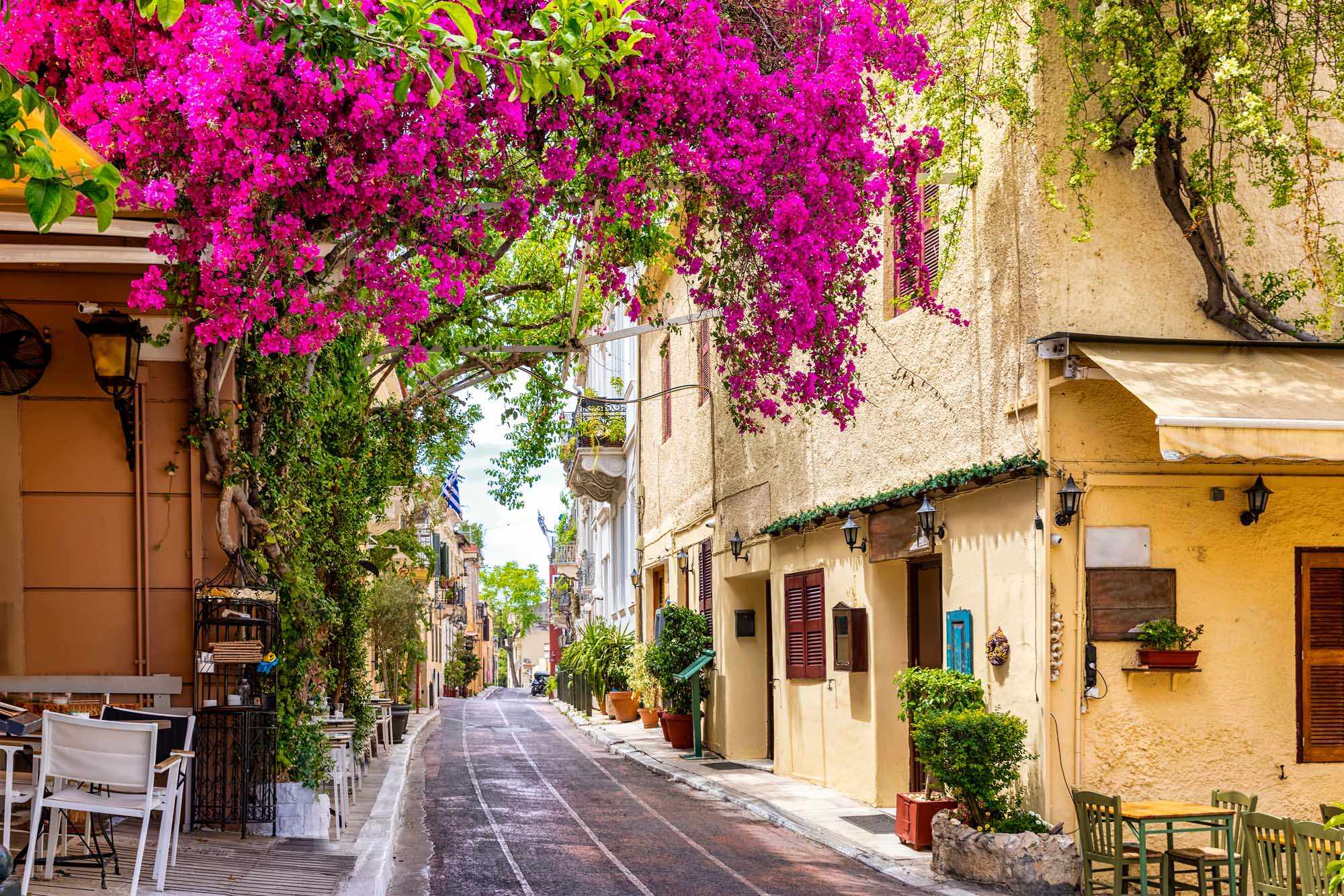 Vibrant magenta bougainvillea cascades over a charming Mediterranean street lined with historic stone buildings