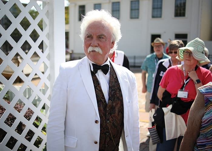 A distinguished gentleman in formal white jacket and bow tie greets passengers during an American