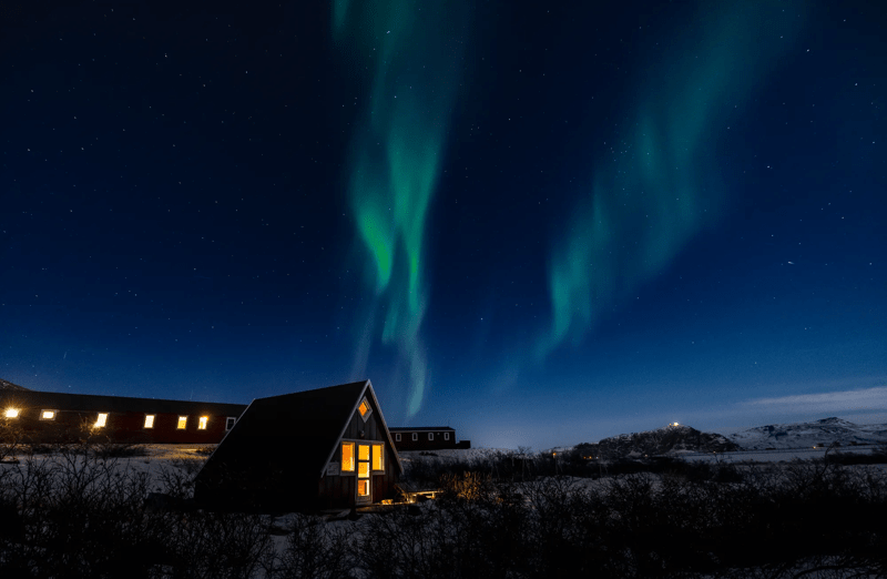 Warmly-lit expedition lodge in Greenland beneath dancing Arctic aurora borealis