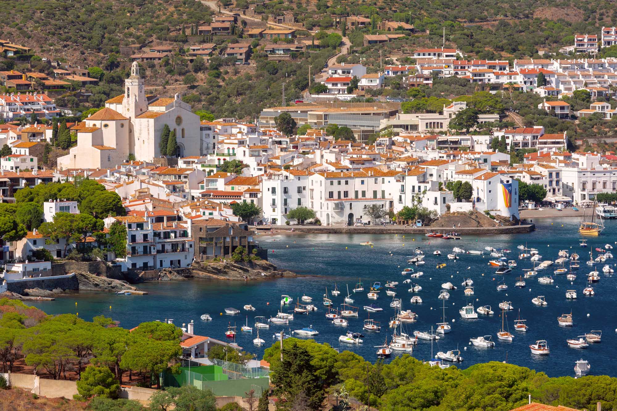 Aerial view of Cadaques harbor with white houses, terracotta roofs, and moored boats along Spain's Costa Brava coastline