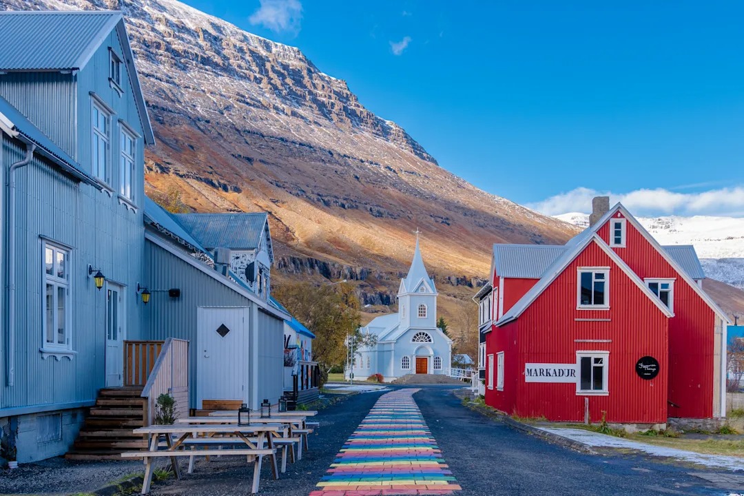 Colorful Icelandic village with traditional houses and white church in dramatic fjord valley