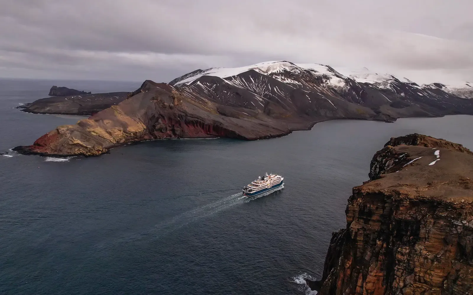 Expedition cruise ship anchored in icy polar waters beneath volcanic peaks