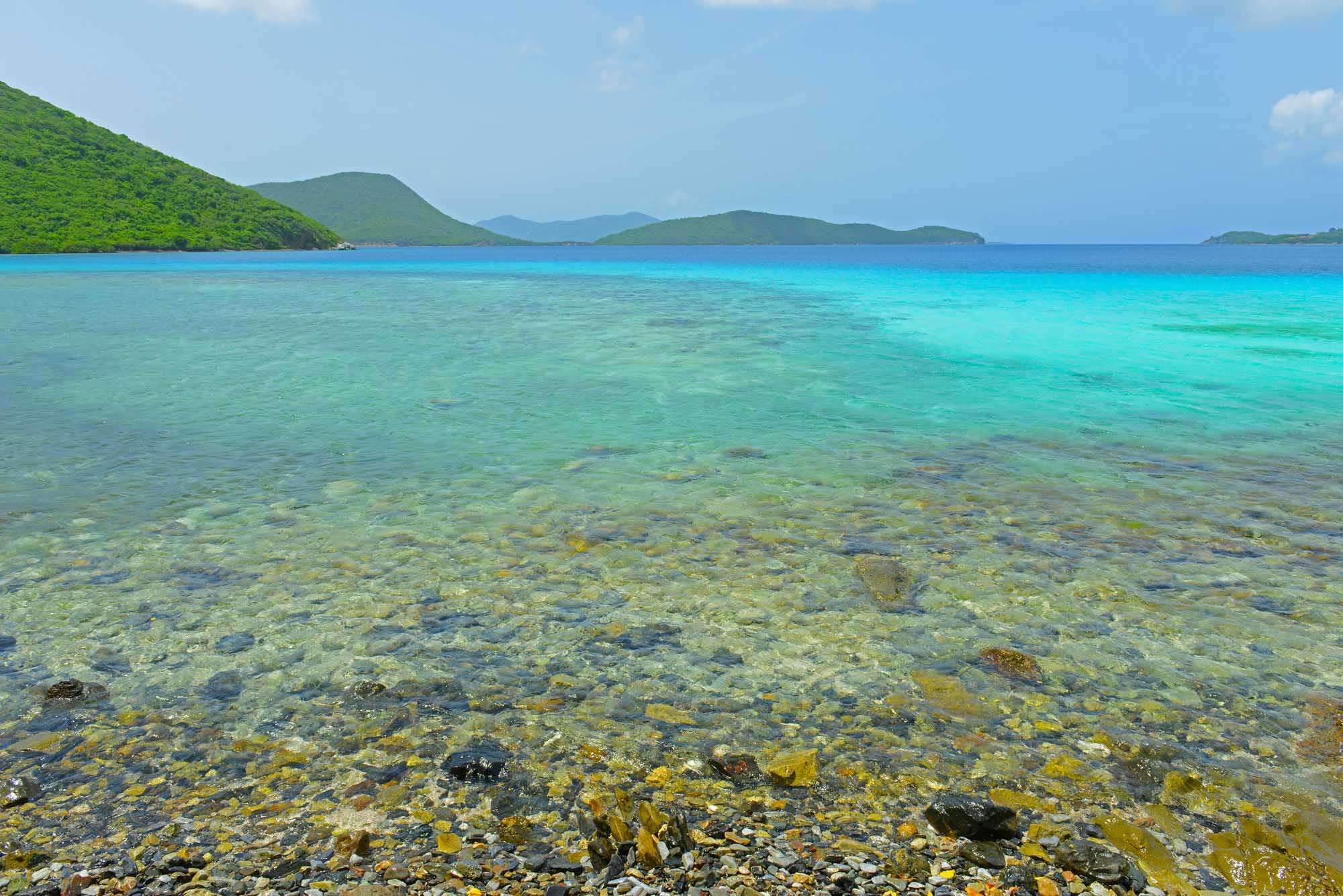 Crystal-clear turquoise waters of Leinster Bay reveal rocky seafloor and lush green hillsides