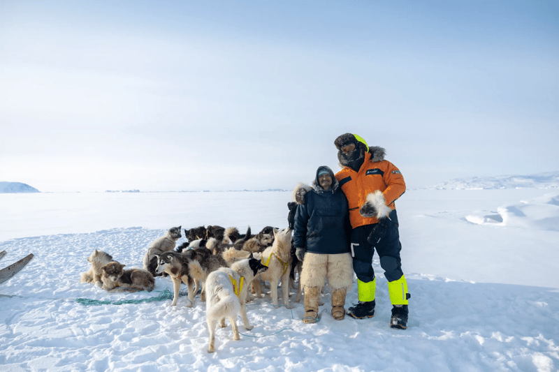 Two travelers with a dog sled team on Greenland sea ice under clear skies