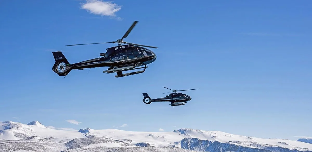 Two helicopters flying in formation over snow-covered mountains of East Antarctica