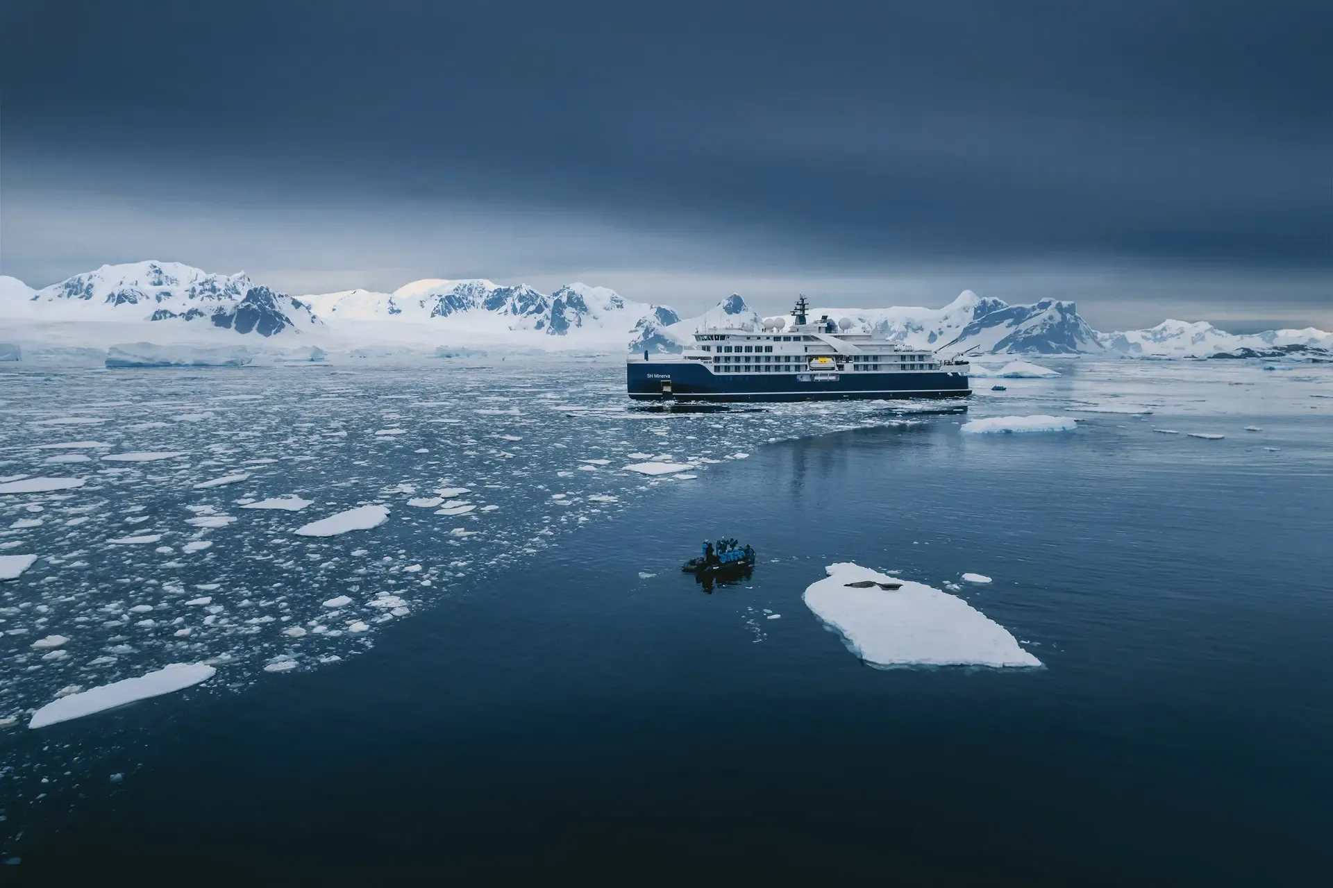 Expedition cruise ship navigating Antarctic waters amid icebergs and zodiac boat