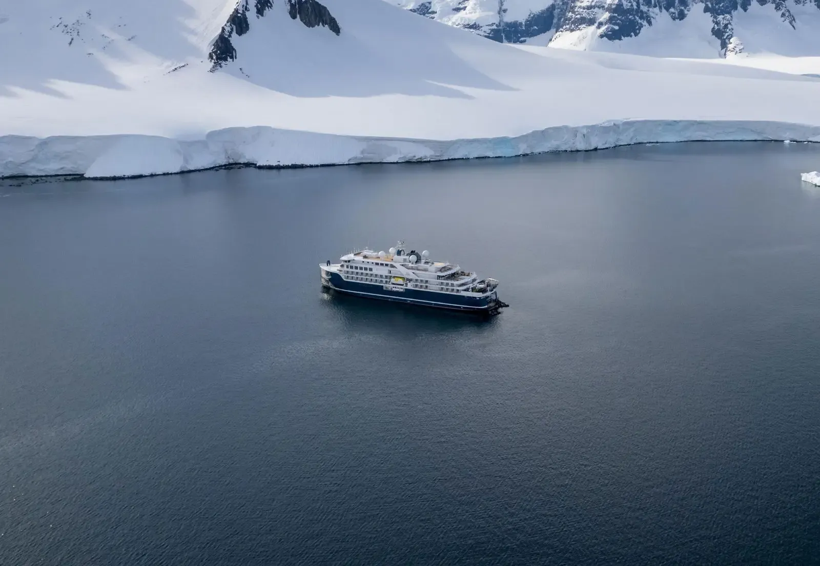 Modern expedition cruise ship anchored in Antarctic waters with ice shelves and snow-covered peaks