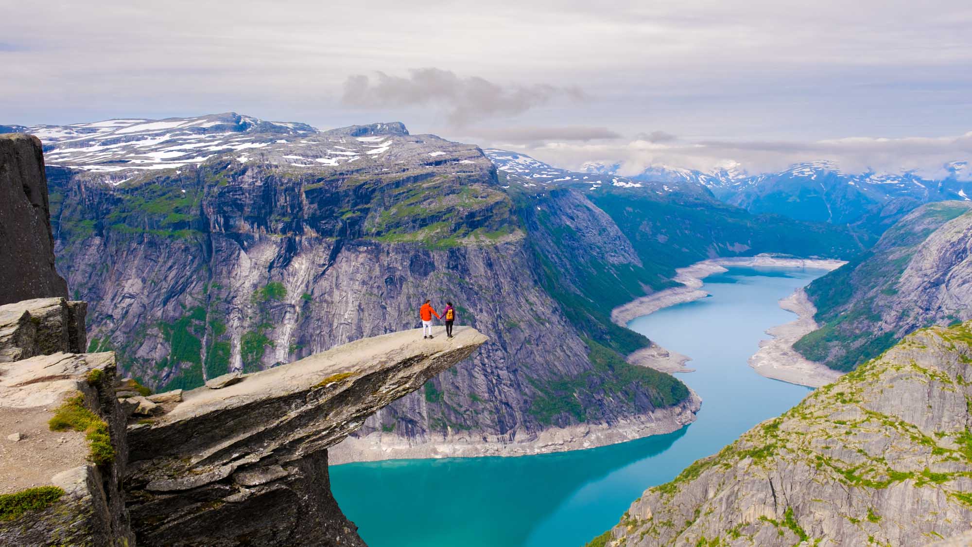 Hikers at Trolltunga Norway Fjord Overlook Two hikers stand on the dramatic cliff edge of Trolltunga in Norway, gazing out over a stunning